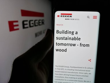 Stuttgart, Almanya - 05-31-2025: Avusturyalı Egger Holzwerkstoffe GmbH şirketinin web sayfası logonun önünde duran kişi. Telefon ekranının merkezine odaklan.