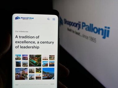 Stuttgart, Almanya - 06-01-2025: Hintli şirket Shapoorji Pallonji Group 'un web sayfası ile logo önünde cep telefonu tutan kişi. Telefon ekranının merkezine odaklan.