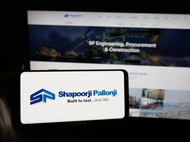 Stuttgart, Almanya - 06-01-2025: Hint firması Shapoorji Pallonji Group 'un logosunun bulunduğu akıllı telefonu web sitesinin önünde tutan kişi. Telefon ekranına odaklan.