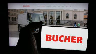 Stuttgart, Almanya - 06-02-2025: İsviçreli makine şirketi Bucher Industries AG 'nin logosuna sahip cep telefonu sahibi kişi web sayfasının önünde ekranda. Telefon ekranına odaklan.