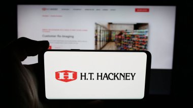Stuttgart, Almanya - 06-02-2025: İnternet sayfası önünde ABD toptan satış şirketi H. T. Hackney Company 'nin logosunu elinde tutan kişi. Telefon ekranına odaklan.
