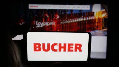 Stuttgart, Almanya - 06-02-2025: İsviçreli makine şirketi Bucher Industries AG 'nin logosunu elinde tutan kişi web sayfasının önünde ekranda. Telefon ekranına odaklan.