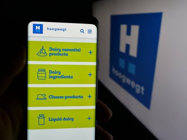 Stuttgart, Almanya - 06-04-2025: Hollandalı mandıra şirketi Hoogwegt Groep B.V. 'nin web sayfası ile logo önünde cep telefonu tutan kişi. Telefon ekranının merkezine odaklan.