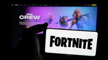 Stuttgart, Almanya - 06-05-2025: İnternet sayfasının önünde ekranda Fortnite oyun platformunun logosu olan cep telefonu tutan kişi. Telefon ekranına odaklan.