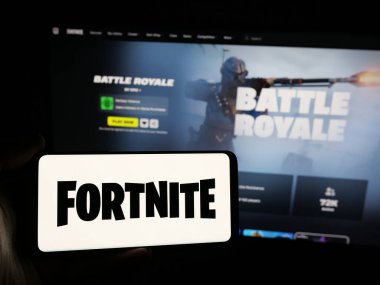 Stuttgart, Almanya - 06-05-2025: İnternet sitesinin önündeki ekranda Fortnite oyun platformunun logosuna sahip akıllı telefonu tutan kişi. Telefon ekranına odaklan.
