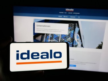 Stuttgart, Almanya - 06-05-2025: İnternet sitesinin önünde ekranda fiyat karşılaştırma şirketi idealo Internet GmbH logosuna sahip akıllı telefonu tutan kişi. Telefon ekranına odaklan.