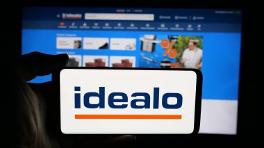 Stuttgart, Almanya - 06-05-2025: İnternet sayfası önünde üzerinde fiyat karşılaştırma şirketi logosu olan cep telefonu sahibi kişi idealo Internet GmbH ekranda. Telefon ekranına odaklan.