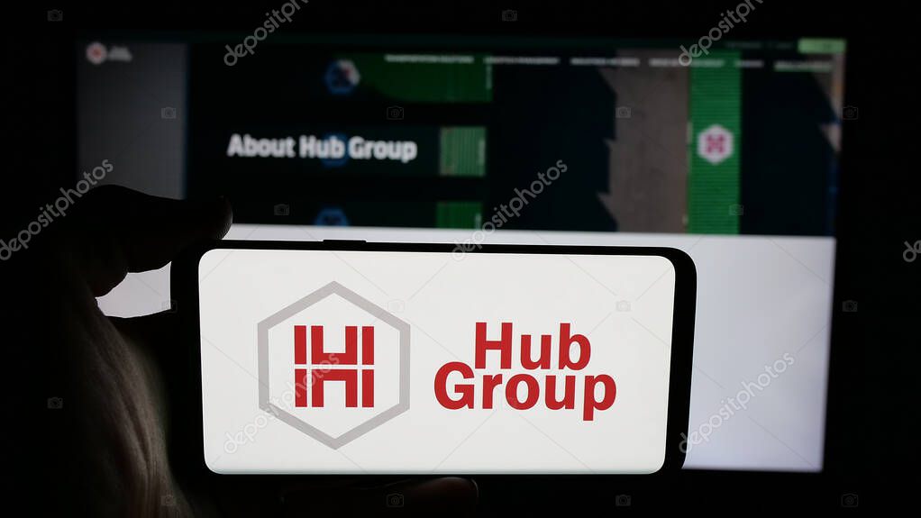 Stuttgart, Germany - 05-31-2025: Person holding cellphone with logo of US logistics company Hub Group Inc. on screen in front of webpage. Focus on phone display.