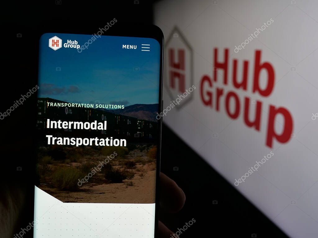 Stuttgart, Germany - 05-31-2025: Person holding cellphone with webpage of US logistics company Hub Group Inc. on screen in front of logo. Focus on center of phone display.