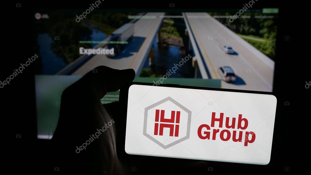 Stuttgart, Germany - 05-31-2025: Person holding mobile phone with logo of US logistics company Hub Group Inc. on screen in front of web page. Focus on phone display.