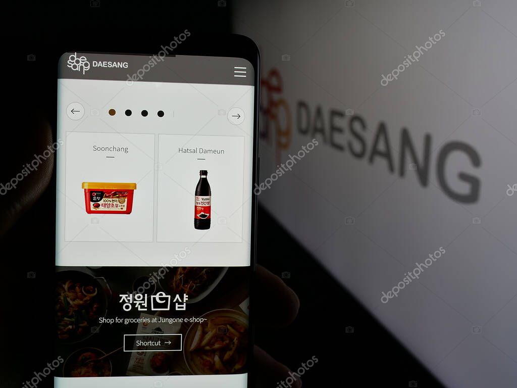 Stuttgart, Germany - 06-01-2025: Person holding cellphone with webpage of Korean food company Daesang Holdings Co. Ltd. on screen in front of logo. Focus on center of phone display.