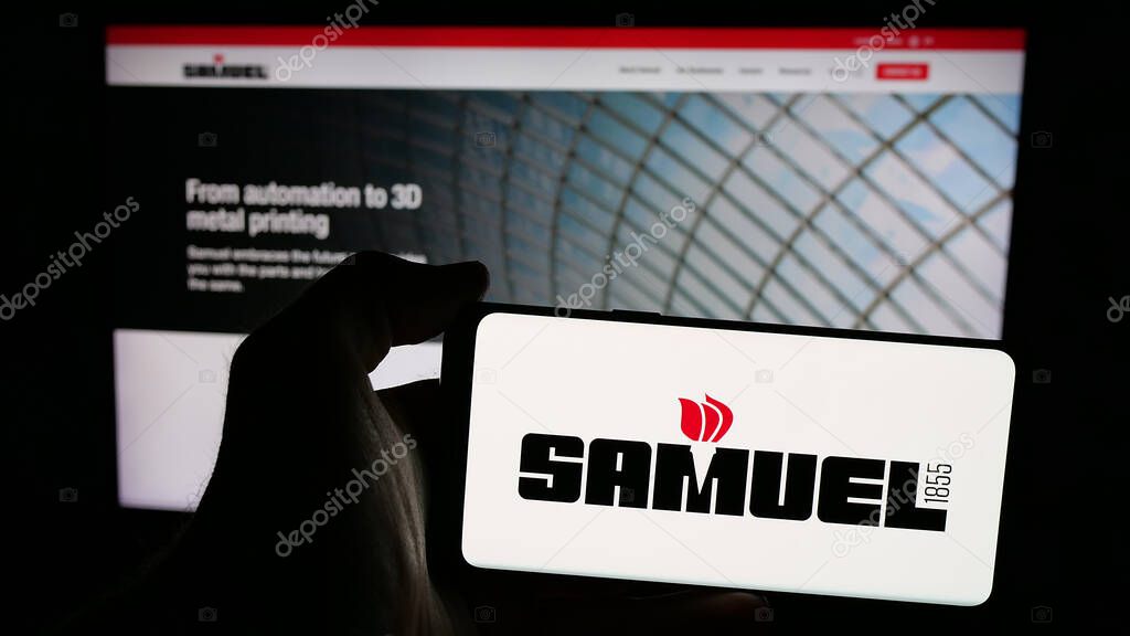 Stuttgart, Germany - 06-02-2025: Person holding mobile phone with logo of metal processing company Samuel Son Co. Inc. on screen in front of web page. Focus on phone display.