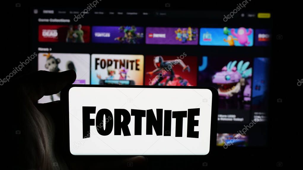 Stuttgart, Germany - 06-05-2025: Person holding cellphone with logo of online video game platform Fortnite on screen in front of webpage. Focus on phone display.