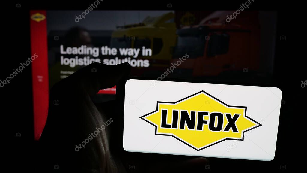 Stuttgart, Germany - 06-05-2025: Person holding mobile phone with logo of Australian logistics company Linfox Pty. Ltd. on screen in front of web page. Focus on phone display.