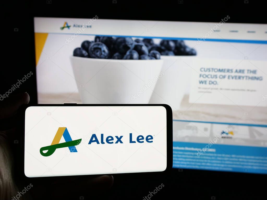 Stuttgart, Germany - 06-05-2025: Person holding smartphone with logo of US grocery wholesale company Alex Lee Inc. on screen in front of website. Focus on phone display.