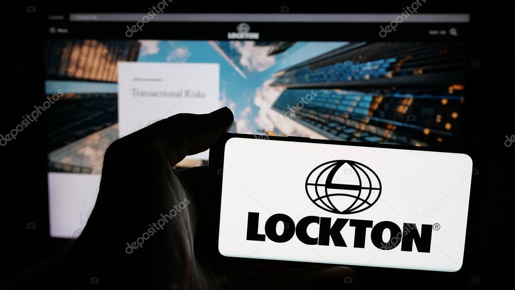 Stuttgart, Germany - 06-05-2025: Person holding mobile phone with logo of financial services company Lockton Companies on screen in front of web page. Focus on phone display.