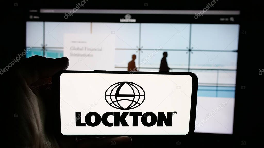 Stuttgart, Germany - 06-05-2025: Person holding cellphone with logo of financial services company Lockton Companies on screen in front of webpage. Focus on phone display.