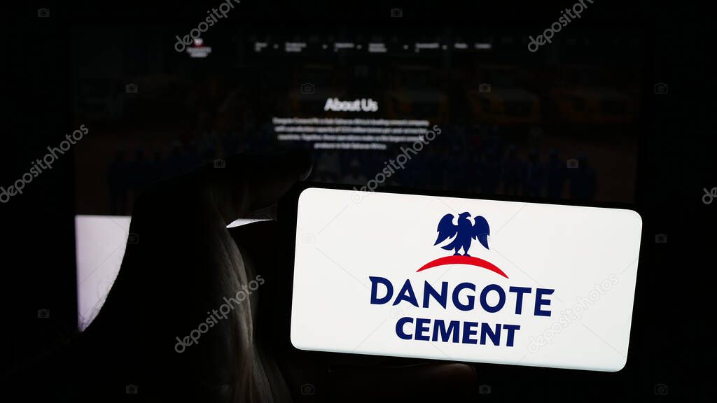 Stuttgart, Germany - 06-05-2025: Person holding mobile phone with logo of Nigerian materials company Dangote Cement plc on screen in front of web page. Focus on phone display.