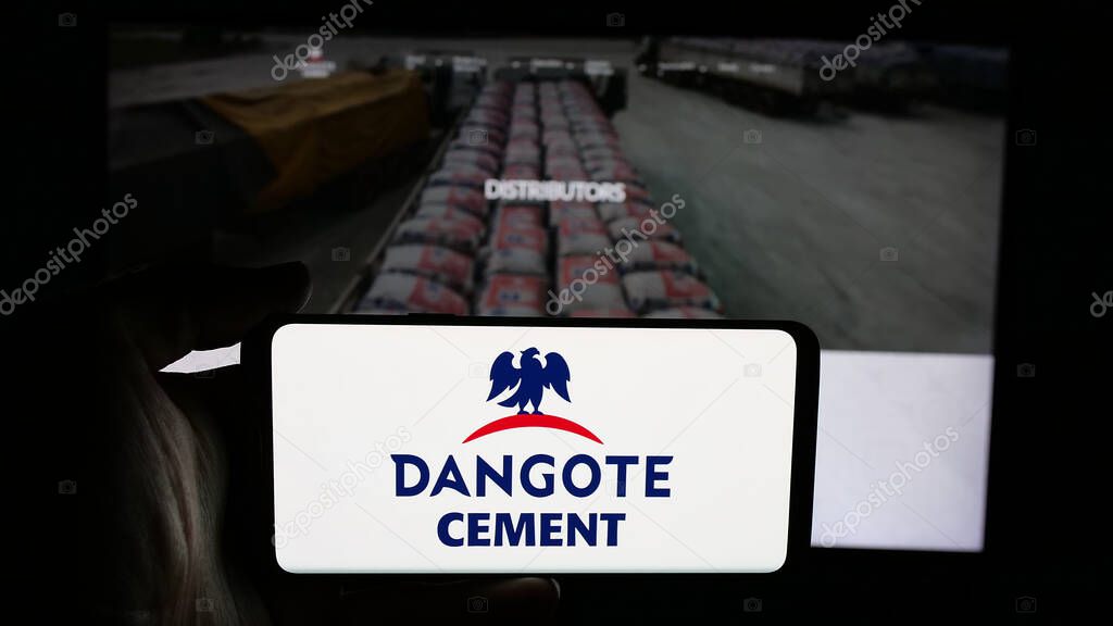 Stuttgart, Germany - 06-05-2025: Person holding cellphone with logo of Nigerian materials company Dangote Cement plc on screen in front of webpage. Focus on phone display.