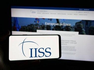 Stuttgart, Almanya - 06-06-2025: İnternet sitesi önünde üzerinde İngiliz Stratejik Çalışmalar Enstitüsü logosu bulunan akıllı telefon sahibi kişi. Telefon ekranına odaklan.