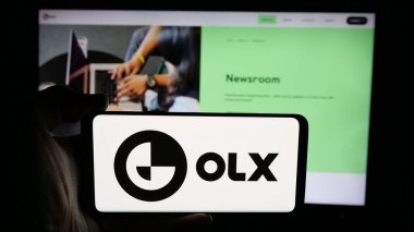 Stuttgart, Almanya - 06-06-2025: Hollandalı pazar şirketi OLX Global B.V. 'nin logosuyla cep telefonu tutan kişi web sayfasının önünde ekranda. Telefon ekranına odaklan.
