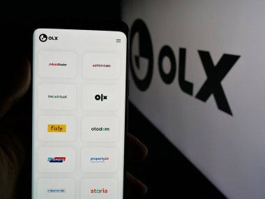 Stuttgart, Almanya - 06-06-2025: Hollandalı pazar şirketi OLX Global B.V. 'nin internet sayfası ile logo önünde cep telefonu tutan kişi. Telefon ekranının merkezine odaklan.