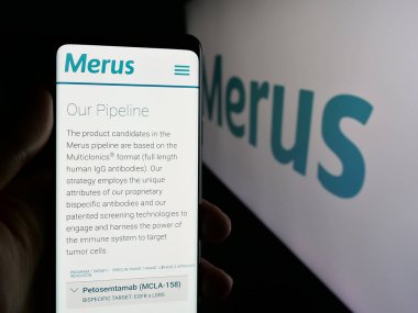 Stuttgart, Almanya - 06-07-2025: Hollandalı biyoteknoloji şirketi Merus NV 'nin web sayfası ile cep telefonu tutan kişi logonun önünde ekranda. Telefon ekranının merkezine odaklan.