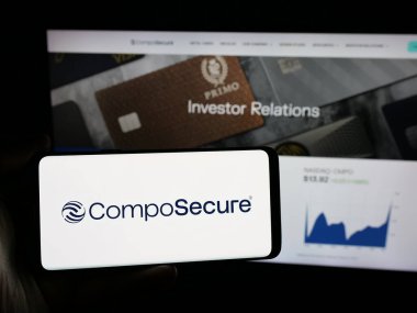 Stuttgart, Almanya - 06-07-2025: İnternet sitesinin önünde üzerinde ABD 'li ödeme kartı şirketi CompoSecure Inc.' in logosu bulunan akıllı telefon sahibi kişi. Telefon ekranına odaklan.