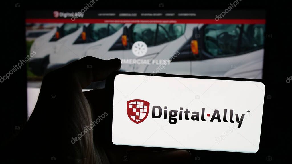 Stuttgart, Germany - 06-07-2025: Person holding mobile phone with logo of US video solutions company Digital Ally Inc. on screen in front of web page. Focus on phone display.