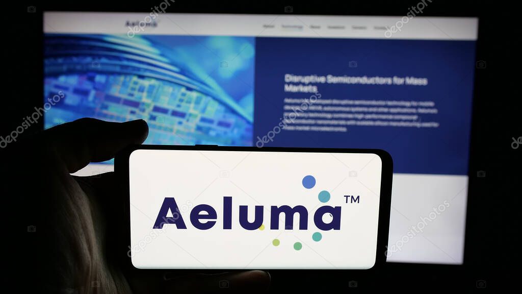 Stuttgart, Germany - 06-07-2025: Person holding cellphone with logo of US semiconductor company Aeluma Inc. on screen in front of webpage. Focus on phone display.