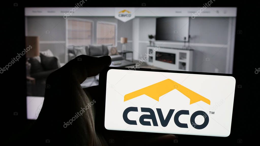 Stuttgart, Germany - 06-07-2025: Person holding mobile phone with logo of US homebuilding company Cavco Industries Inc. on screen in front of web page. Focus on phone display.