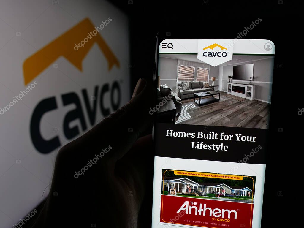 Stuttgart, Germany - 06-07-2025: Person holding smartphone with web page of US homebuilding company Cavco Industries Inc. on screen in front of logo. Focus on center of phone display.