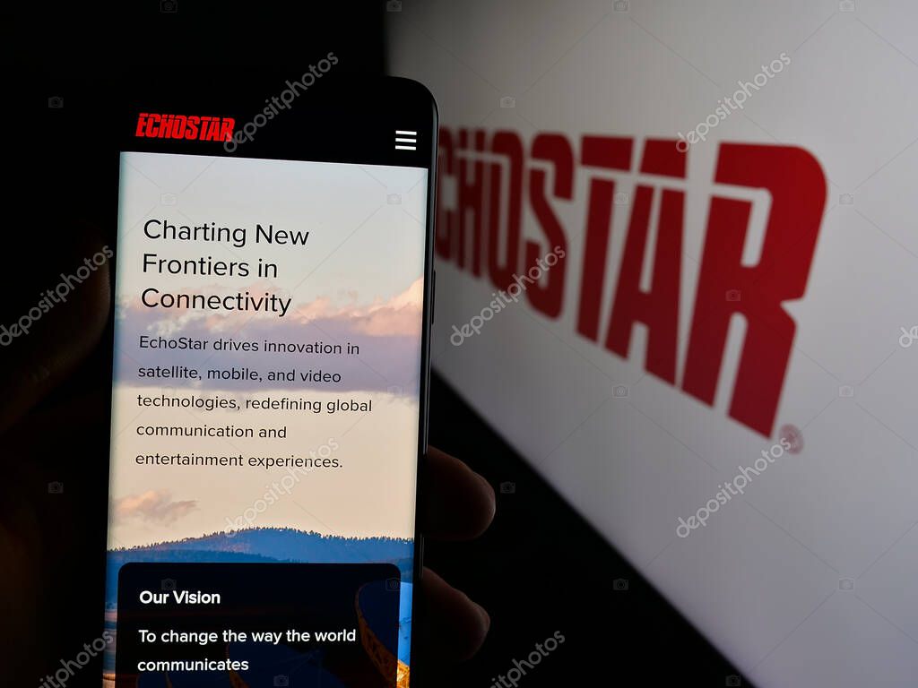 Stuttgart, Germany - 06-07-2025: Person holding cellphone with webpage of US telecom company EchoStar Corporation on screen in front of logo. Focus on center of phone display.