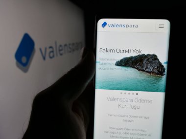 Stuttgart, Almanya - 06-08-2025: Türk şirketi ValensPara Odeme Kurulusu 'nun internet sayfası ile cep telefonu tutan kişi logonun önünde ekranda görülüyor. Telefon ekranının merkezine odaklan.