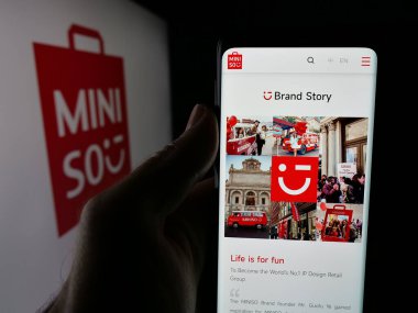 Stuttgart, Almanya - 06-09-2025: Perakende şirketi MINISO Group Holding Limited 'in web sayfası olan cep telefonu logonun önünde ekranda. Telefon ekranının merkezine odaklan.