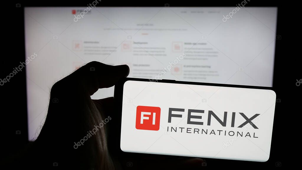 Stuttgart, Germany - 06-08-2025: Person holding mobile phone with logo of Fenix International Limited (OnlyFans) on screen in front of web page. Focus on phone display.