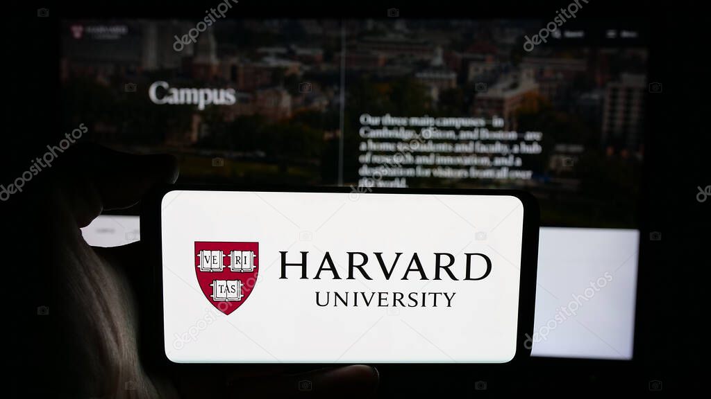 Stuttgart, Germany - 06-09-2025: Person holding cellphone with logo of US research institution Harvard University on screen in front of webpage. Focus on phone display.