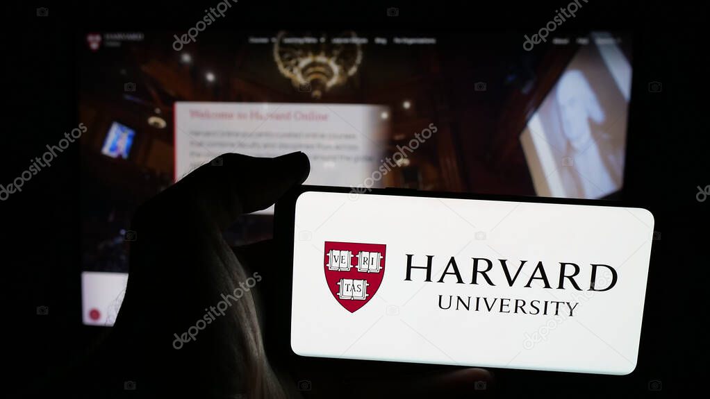 Stuttgart, Germany - 06-09-2025: Person holding mobile phone with logo of US research institution Harvard University on screen in front of web page. Focus on phone display.