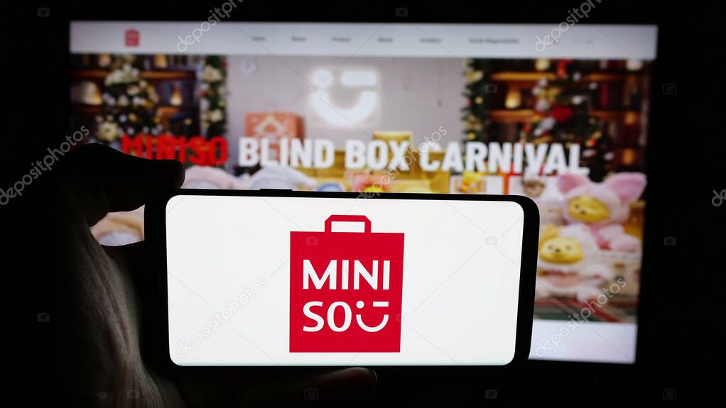 Stuttgart, Germany - 06-09-2025: Person holding cellphone with logo of retail company MINISO Group Holding Limited on screen in front of webpage. Focus on phone display.
