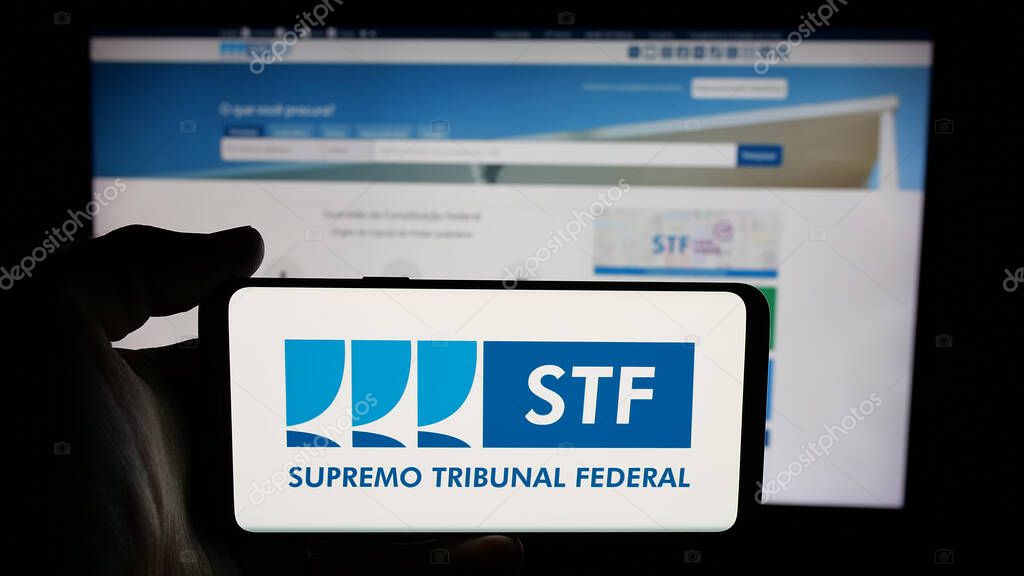 Stuttgart, Germany - 06-09-2025: Person holding cellphone with logo of Brazil court Supremo Tribunal Federal (STF) on screen in front of webpage. Focus on phone display.