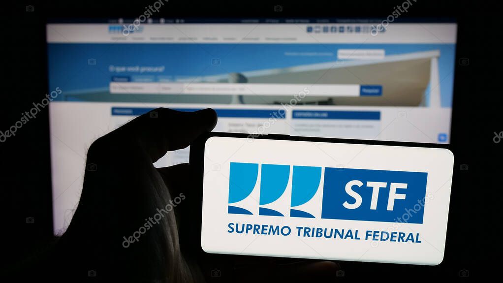 Stuttgart, Germany - 06-09-2025: Person holding mobile phone with logo of Brazil court Supremo Tribunal Federal (STF) on screen in front of web page. Focus on phone display.