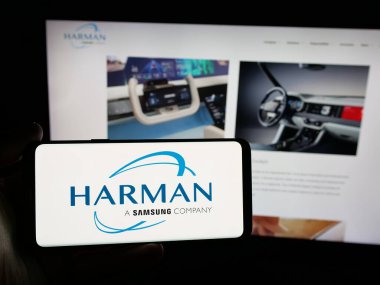 Stuttgart, Almanya - 06-11-2025: Web sitesi önünde ekranda Harman International Industries Inc. şirketinin logosunu taşıyan kişi. Telefon ekranına odaklan.