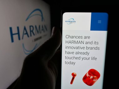 Stuttgart, Almanya - 06-11-2025: Logo önünde ekranda Harman International Industries Inc. şirketinin web sayfası bulunan kişi. Telefon ekranının merkezine odaklan.