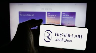 Stuttgart, Almanya - 06-13-2025: Suudi Arabistan havayolu şirketi Riyad Air 'in logosunun bulunduğu cep telefonu sahibi kişi web sitesinin önünde ekranda. Telefon ekranına odaklan.