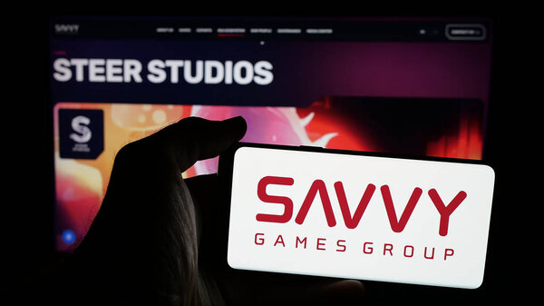 Stuttgart, Germany - 06-13-2025: Person holding mobile phone with logo of Saudi video games company Savvy Games Group on screen in front of web page. Focus on phone display.