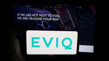 Stuttgart, Almanya - 06-14-2025: İnternet sayfası önünde üzerinde Elektrikli Araç Altyapı Şirketi EVIQ logosu bulunan cep telefonu sahibi kişi. Telefon ekranına odaklan.