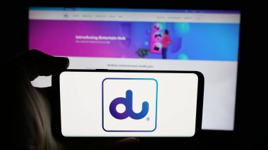 Stuttgart, Almanya - 06-18-2025: İnternet sayfası önünde Emirates Entegre Telekomünikasyon (du) logosu olan cep telefonu sahibi kişi. Telefon ekranına odaklan.