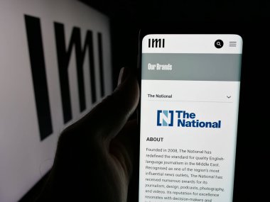Stuttgart, Almanya - 06-18-2025: Uluslararası Medya Yatırımları (IMI) şirketinin web sayfası logonun önünde duran kişi. Telefon ekranının merkezine odaklan.