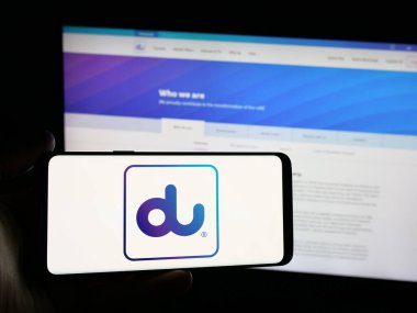 Stuttgart, Almanya - 06-18-2025: İnternet sitesi önünde üzerinde Emirates Entegre Telekomünikasyon (du) logosu bulunan kişi. Telefon ekranına odaklan.