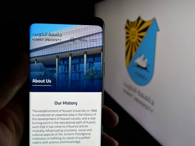 Stuttgart, Almanya - 06-19-2025: Eðitim Kurumu Kuveyt Üniversitesi 'nin web sayfası logo önünde ekranda olan cep telefonu sahibi kişi. Telefon ekranının merkezine odaklan.